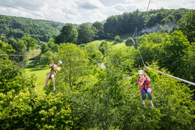 Man and woman zip lining over a green field.