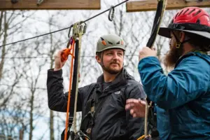 two men wearing helmets on a challenge course platform wearing during training