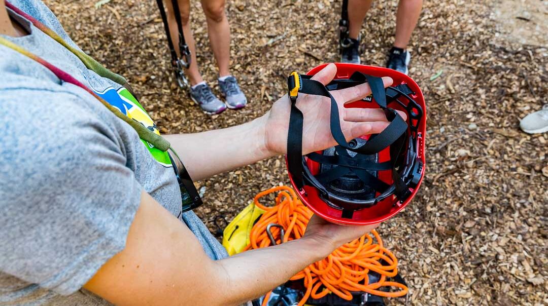 trainer inspecting a helmet and other challenge course safety equipment