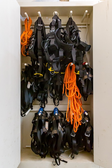 Challenge course PPE storage with harnesses and lanyards organized on racks during ACCT-accredited inspection