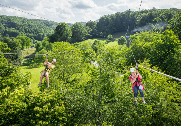 Man and woman zip lining over a green field.